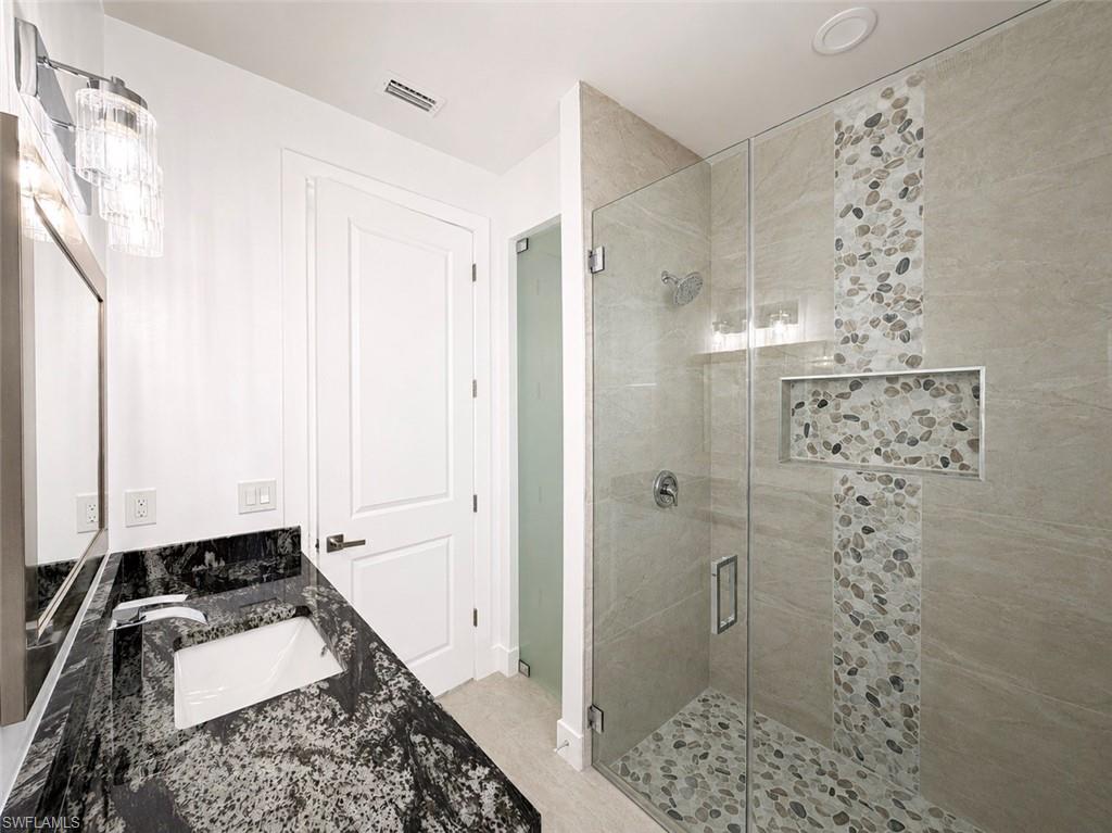 Modern bathroom featuring a frameless glass shower enclosure with pebble tile accents
