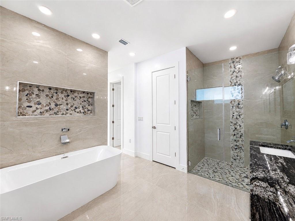 Modern bathroom featuring a freestanding tub, glass-enclosed shower, and a vanity with a dark stone countertop