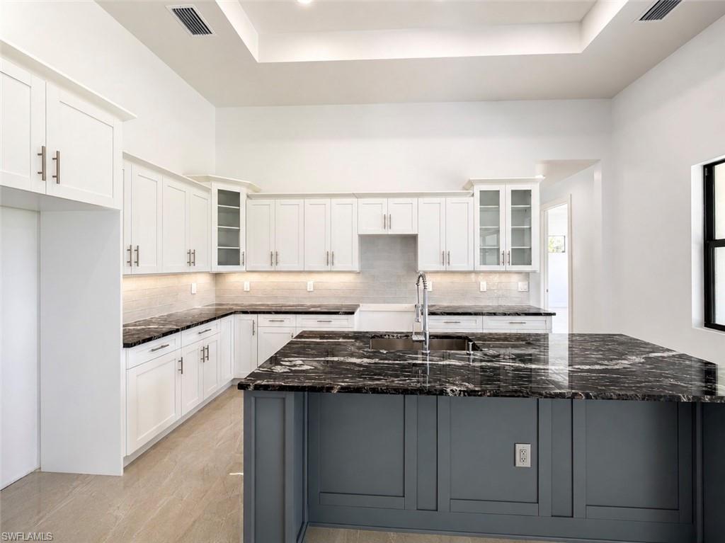 Modern kitchen featuring an expansive island with a built-in sink and dark veined countertop, complemented by white cabinetry with glass-front accents