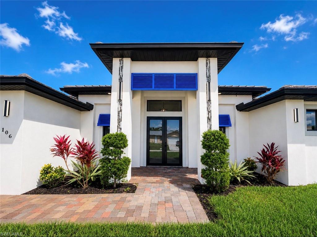Modern exterior featuring a prominent covered entry with double glass doors, a paver walkway, contemporary sconce lighting, and decorative blue awnings