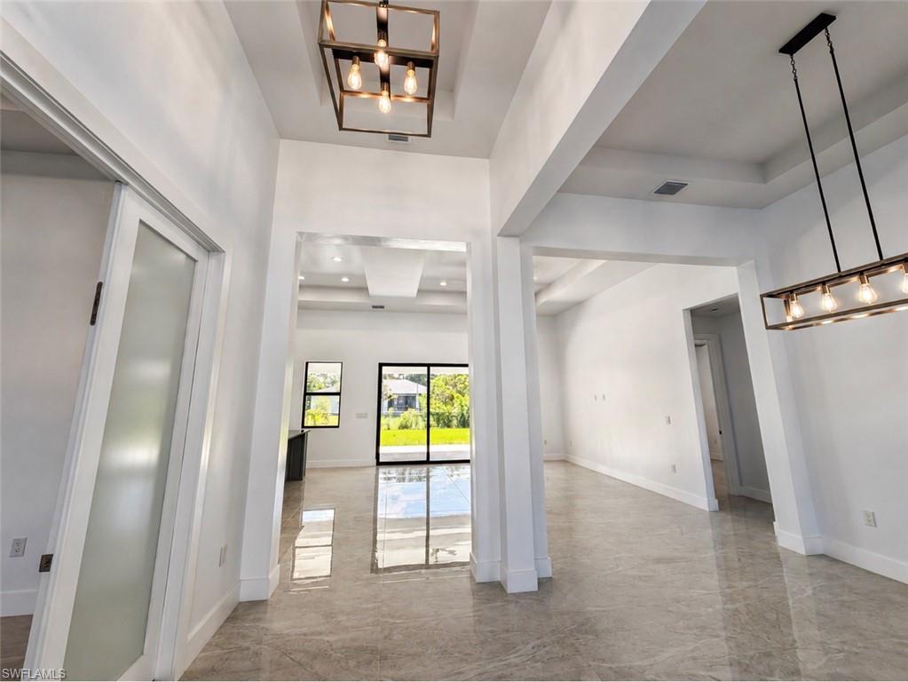 Spacious interior with polished large format tile flooring, contemporary lighting fixtures, high ceilings, tray ceiling details, and a sliding glass door leading to the exterior