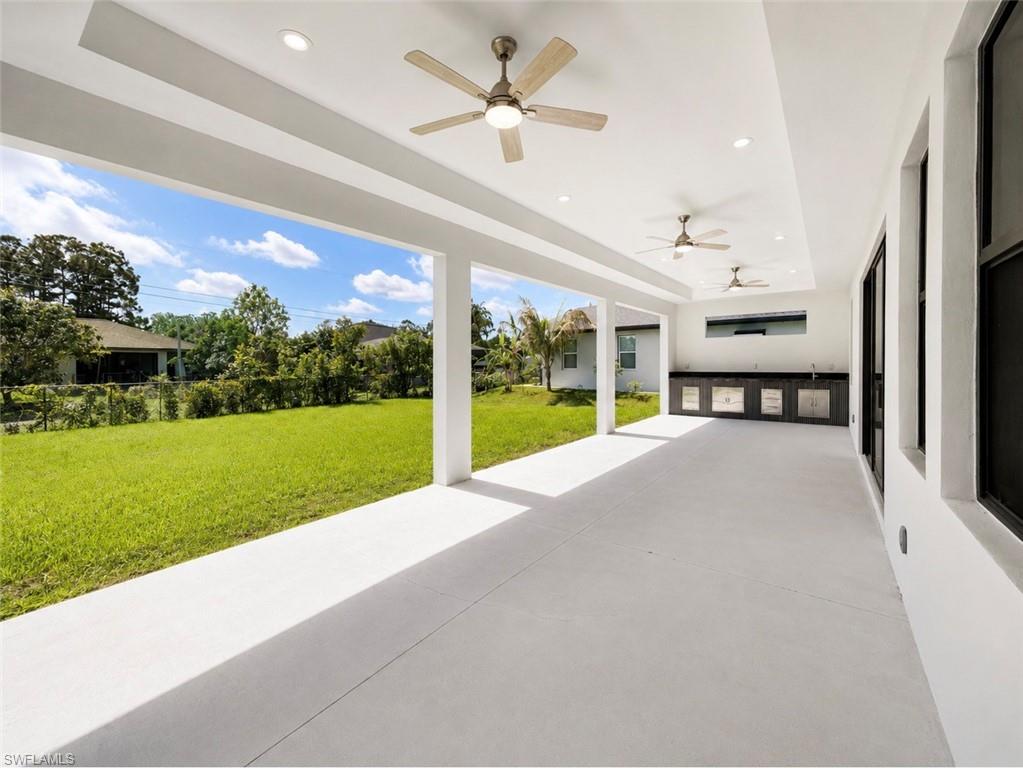 Spacious covered patio with a built-in outdoor kitchen, featuring a sink, dark cabinetry, and light countertops