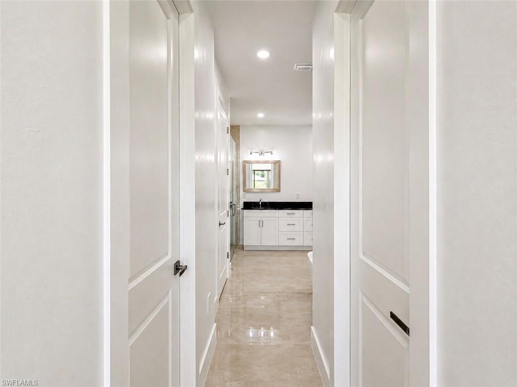Hallway featuring white paneled doors with dark hardware, recessed lighting, and polished tile flooring