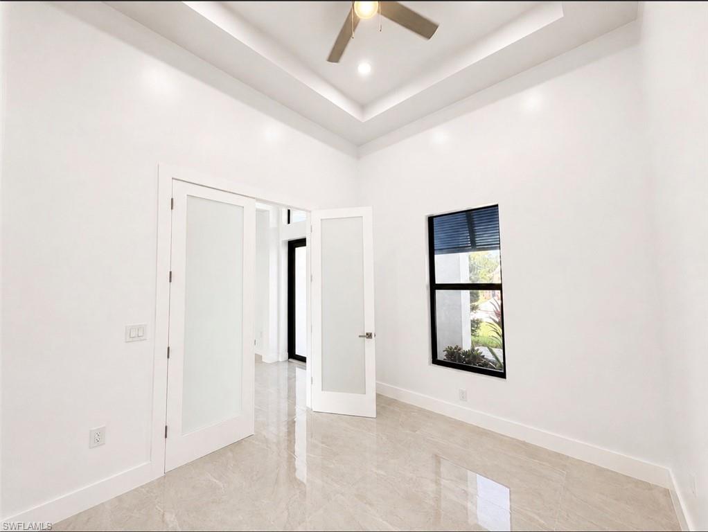 Bright room featuring white walls, a tray ceiling with recessed lighting, and a ceiling fan