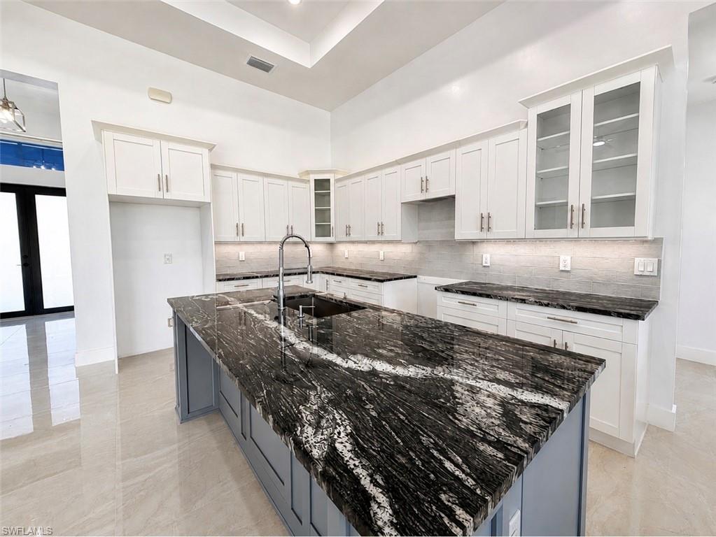 Kitchen featuring a large central island with a dramatic veined countertop, an undermount sink, and a gooseneck faucet