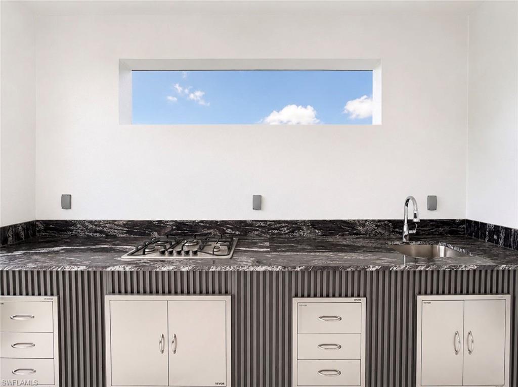 Outdoor kitchen featuring a built-in gas cooktop, undermount stainless steel sink with a high-arc faucet, and dark granite countertops