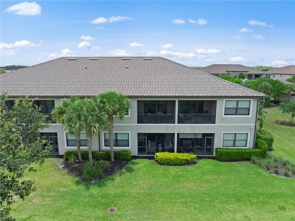 Two-story stucco property featuring a tile roof, mature palm trees, and screened balconies