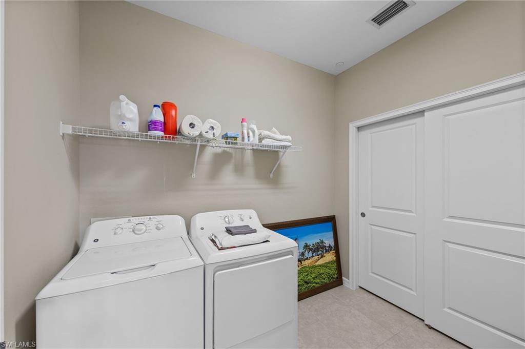 Dedicated laundry area featuring light neutral wall paint, tiled flooring, white wire shelving, and white sliding closet doors