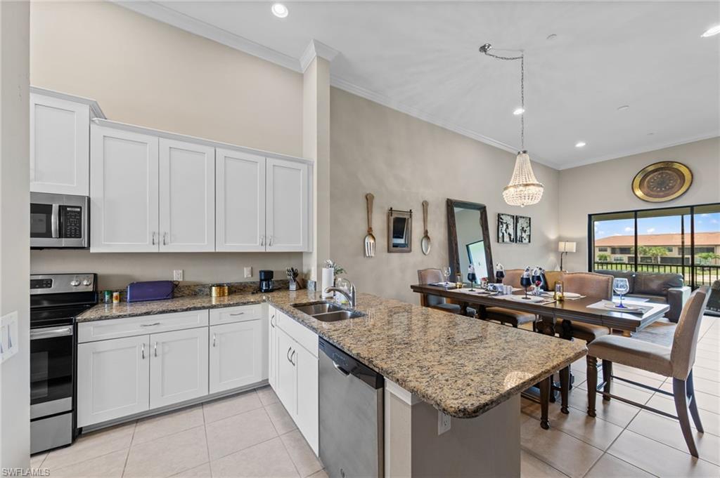 Open-concept kitchen and dining area featuring white shaker cabinetry, granite countertops, tile flooring, and stainless steel appliances