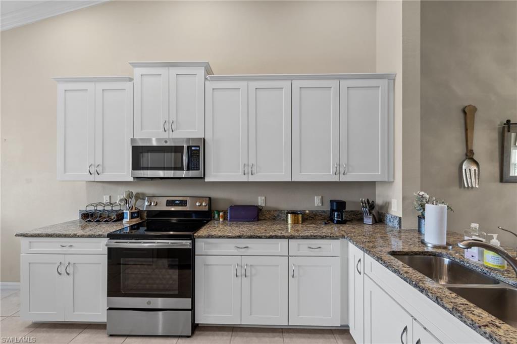Kitchen featuring white shaker-style cabinetry, granite countertops, and stainless steel appliances including an oven range and built-in microwave