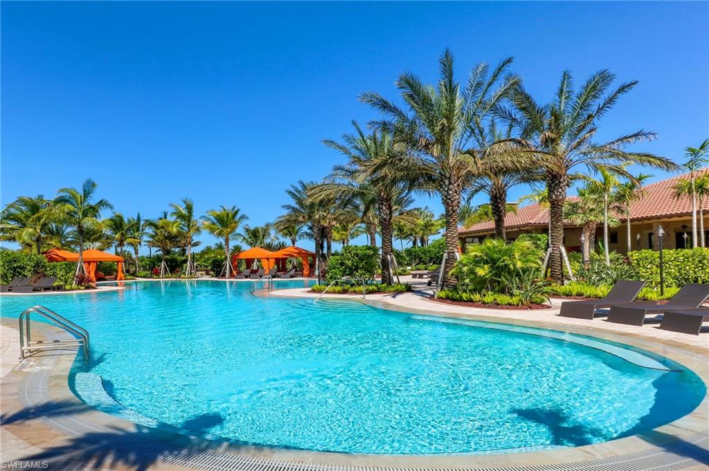 Curved swimming pool with integrated steps, surrounded by a light-toned paved deck and lush tropical landscaping