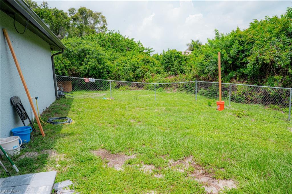 Grassy backyard area featuring a chain-link fence and mature perimeter landscaping