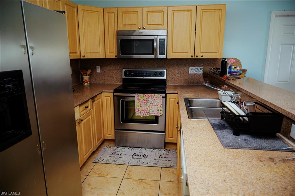 Kitchen featuring light wood cabinetry, stainless steel appliances, stone-finish countertops, and a tile floor