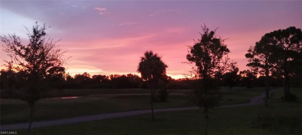 Expansive golf course scenery featuring mature trees, a palm tree, and a serene water feature under a colorful sky