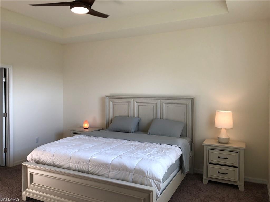 Spacious sleeping area featuring a tray ceiling, ceiling fan with integrated lighting, neutral wall tones, and carpet flooring