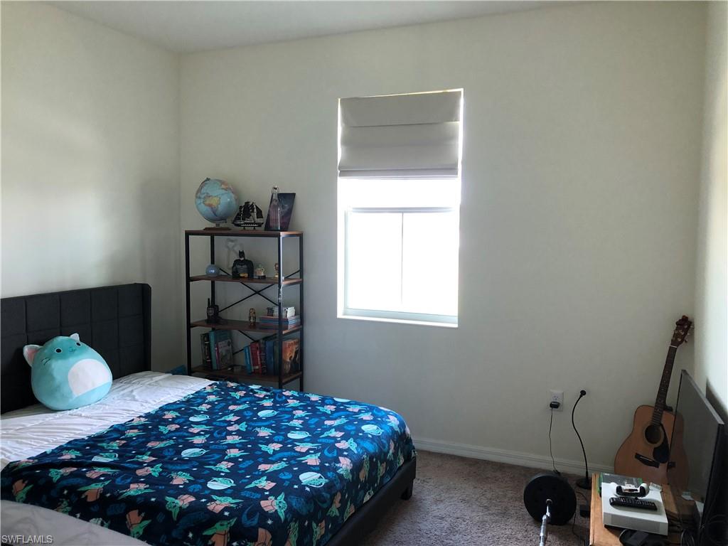 Light-filled interior space featuring a single window with Roman shades, neutral-toned walls, and carpet flooring