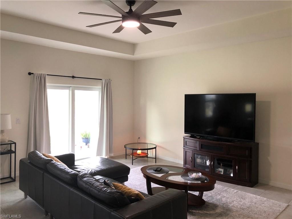 Living area featuring a tray ceiling with a dark-bladed ceiling fan, sliding glass doors to the exterior, and light-toned tile flooring