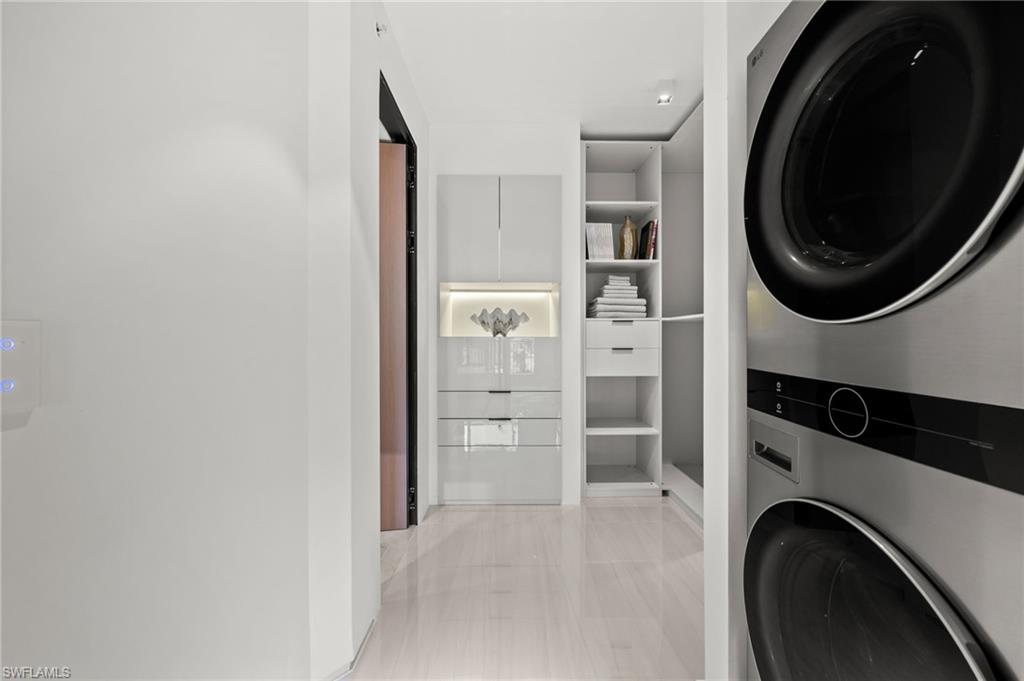 Integrated laundry center featuring a stacked washer and dryer, light wood-finish flooring, built-in shelving, recessed lighting, and a contemporary light switch panel