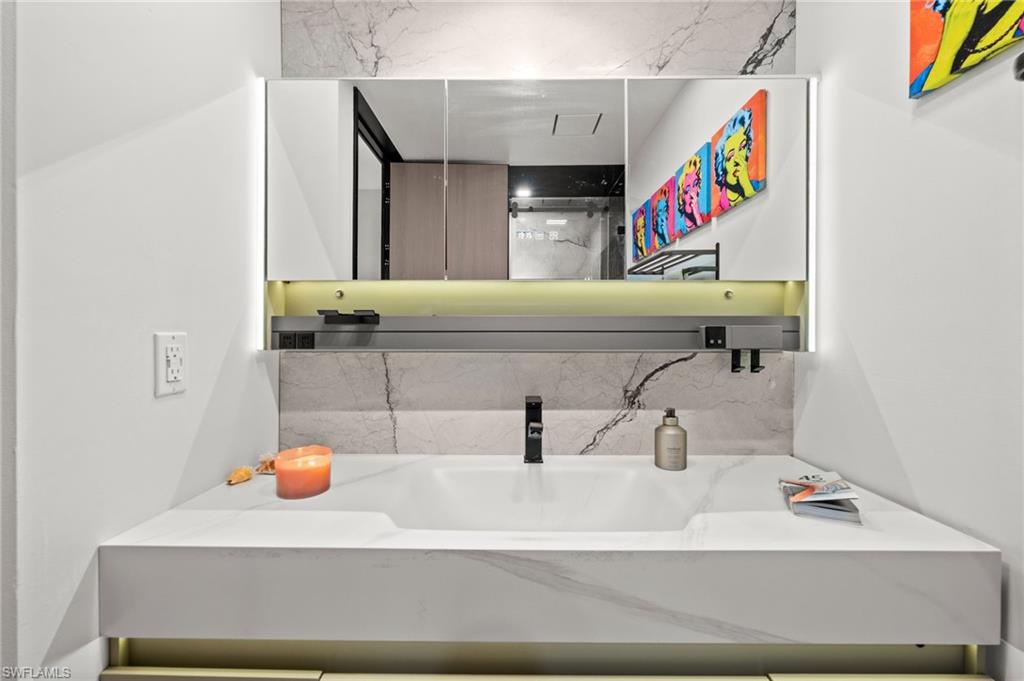 Vanity featuring an integrated sink with a matte black faucet, a mirrored medicine cabinet with integrated lighting, and a marble-finish countertop and backsplash
