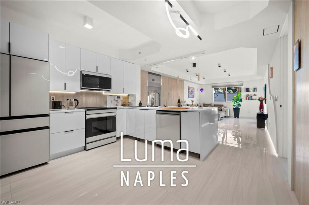 Contemporary kitchen featuring high-gloss white cabinetry, integrated stainless steel appliances, a center island with a built-in dishwasher, and light-toned tile flooring