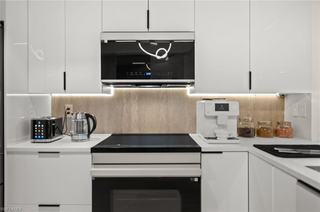 Modern kitchen featuring sleek white cabinetry with black hardware, a built-in oven, and a flat cooktop