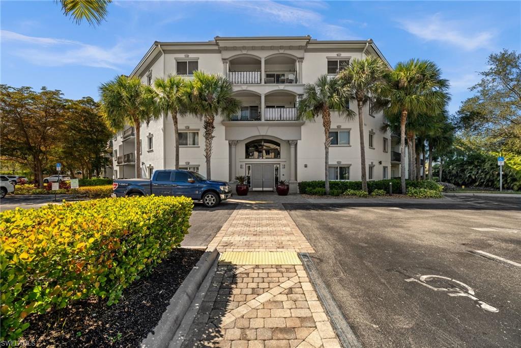 Multi-story building exterior featuring a neutral stucco finish, multiple balconies with dark railings, and a prominent arched entryway
