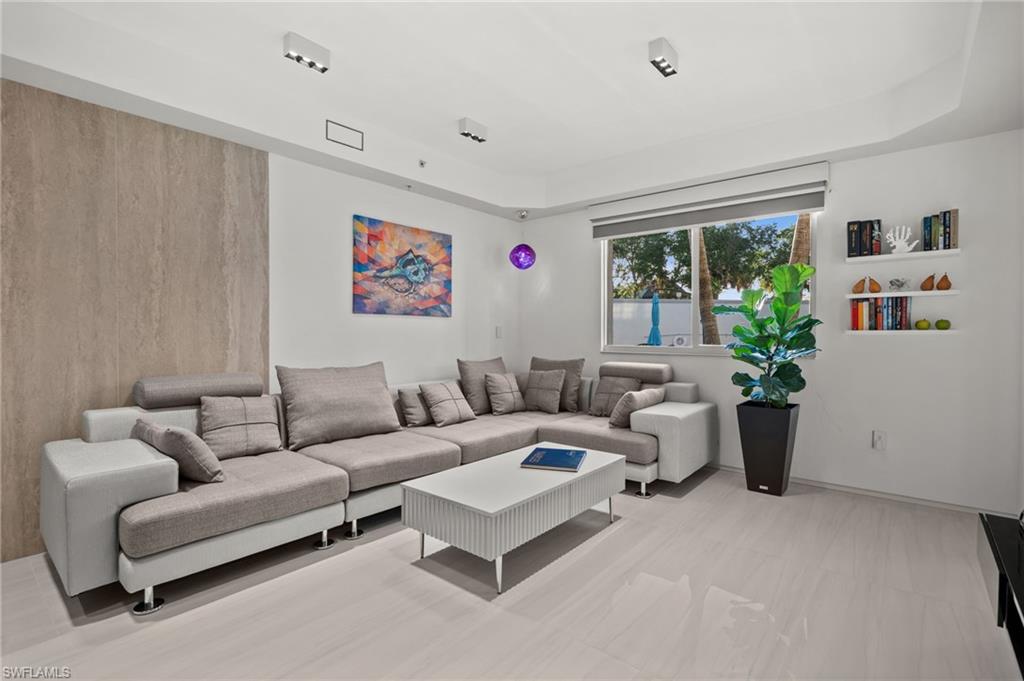 Bright living space featuring sleek light-toned flooring, a textured accent wall, recessed lighting, a large window, and integrated shelving