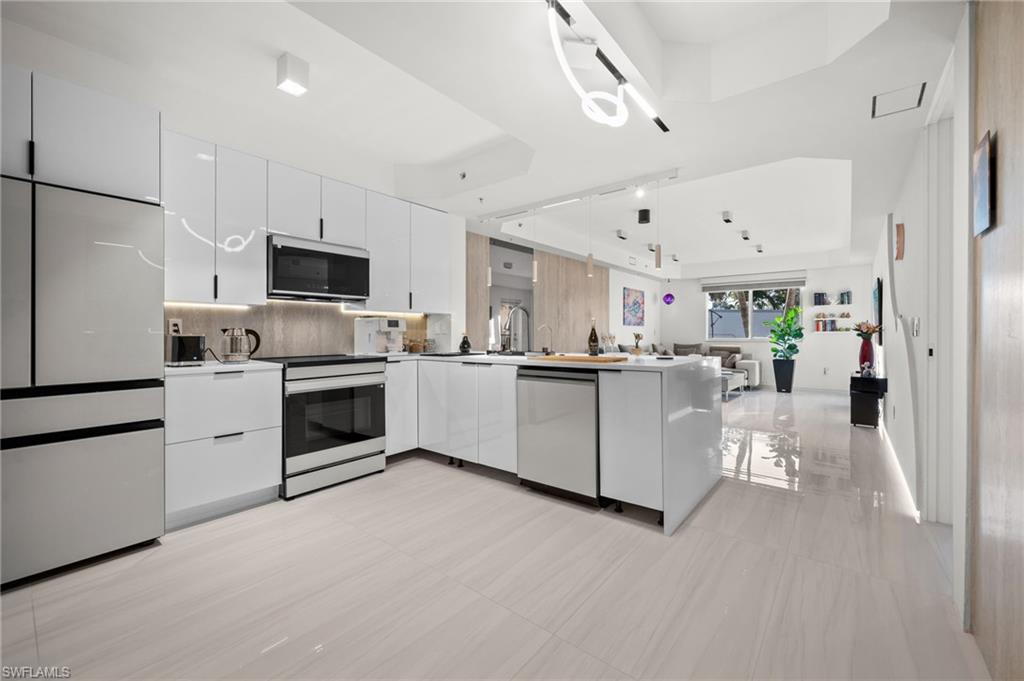 Modern kitchen featuring white high-gloss cabinetry, stainless steel appliances, and wood-finish flooring