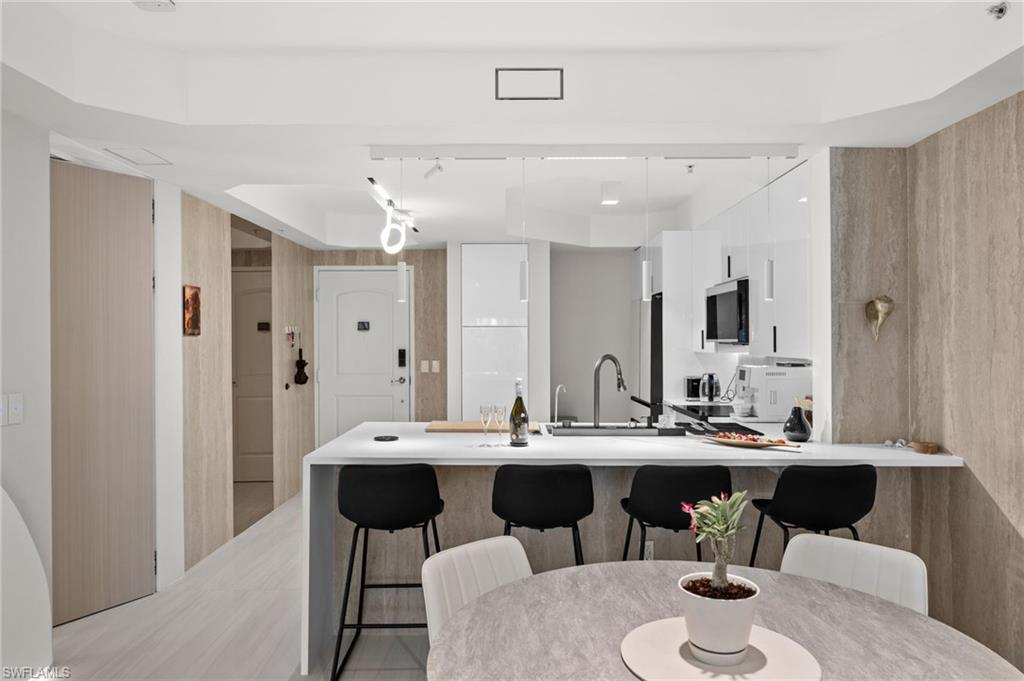 Modern kitchen featuring a waterfall island with integrated seating, white cabinetry, and stainless steel appliances