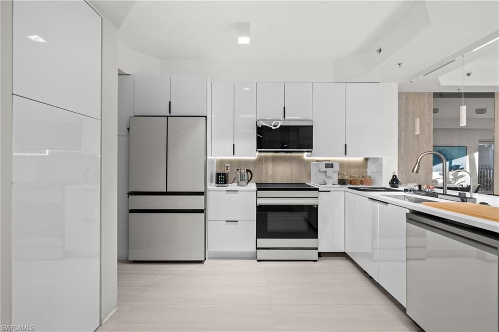 Contemporary kitchen featuring white high-gloss cabinetry, stainless steel appliances, and integrated under-cabinet lighting