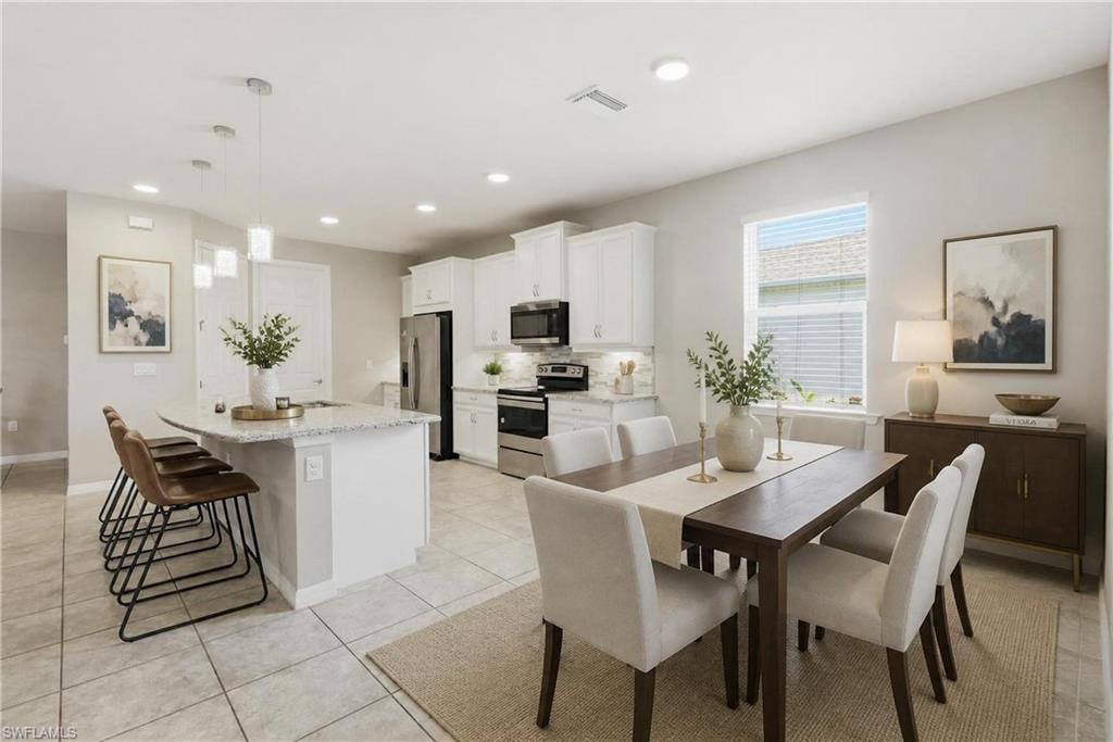 Open-concept living space featuring a kitchen island with pendant lighting, white cabinetry, stainless steel appliances, and a dining area with a window