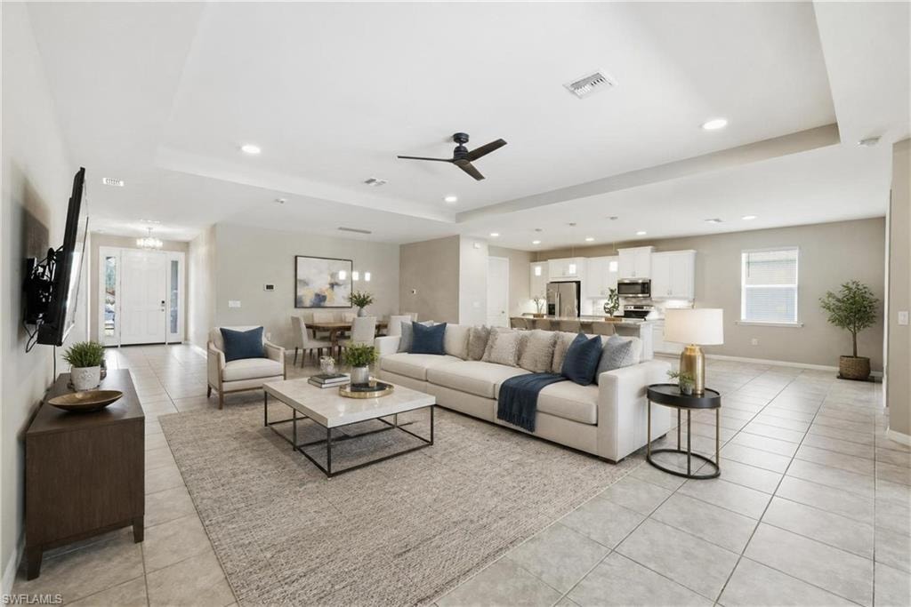 Expansive open-concept living area featuring a tray ceiling with a ceiling fan, recessed lighting, and large format tile flooring