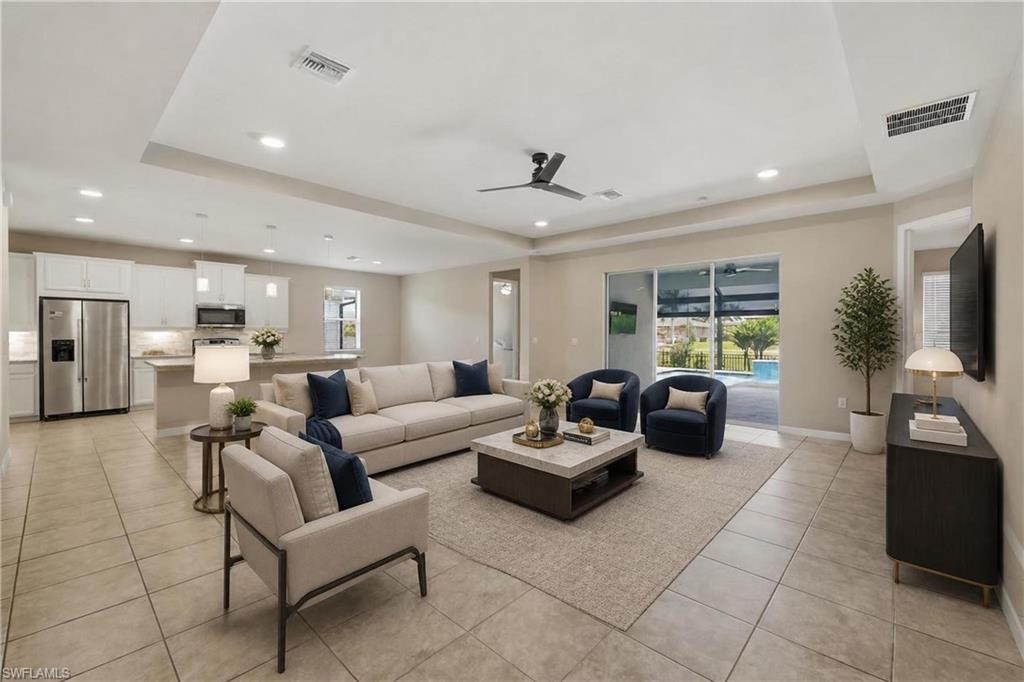 Spacious open-concept living area featuring neutral-toned tile flooring throughout, a tray ceiling with recessed lighting, and a contemporary ceiling fan