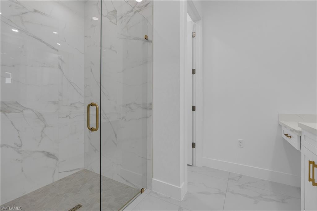 Glass-enclosed shower with large format tile walls and flooring, featuring brass hardware