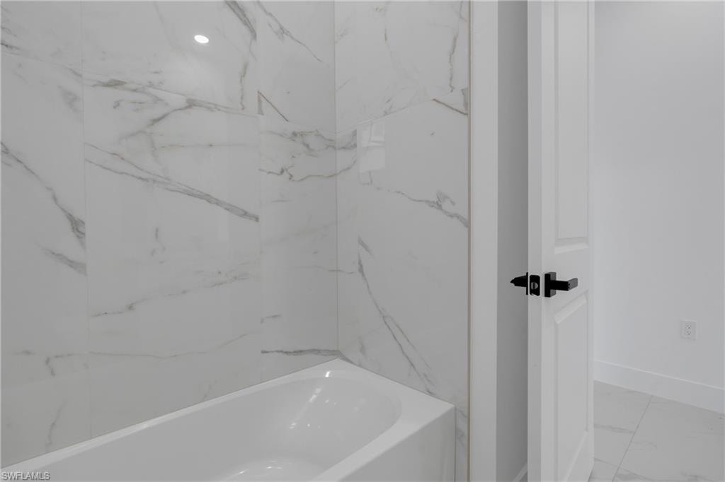 White soaking tub with large format marble-look tile surround