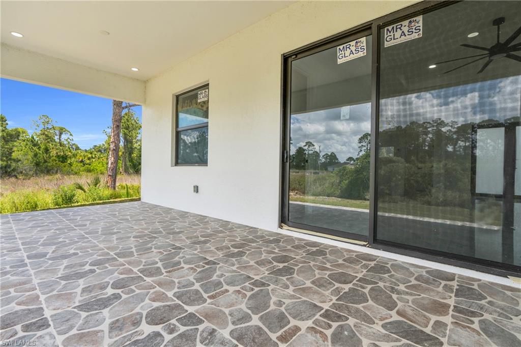 Covered patio featuring irregular-patterned stone-look tile flooring, white stucco walls, recessed lighting, and a black ceiling fan