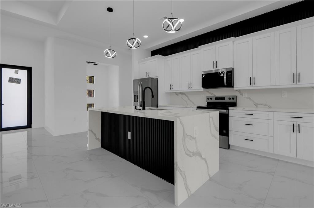 Modern kitchen featuring white shaker cabinetry with matte black hardware, integrated stainless steel appliances, a waterfall island with a fluted black base, and a tiled backsplash