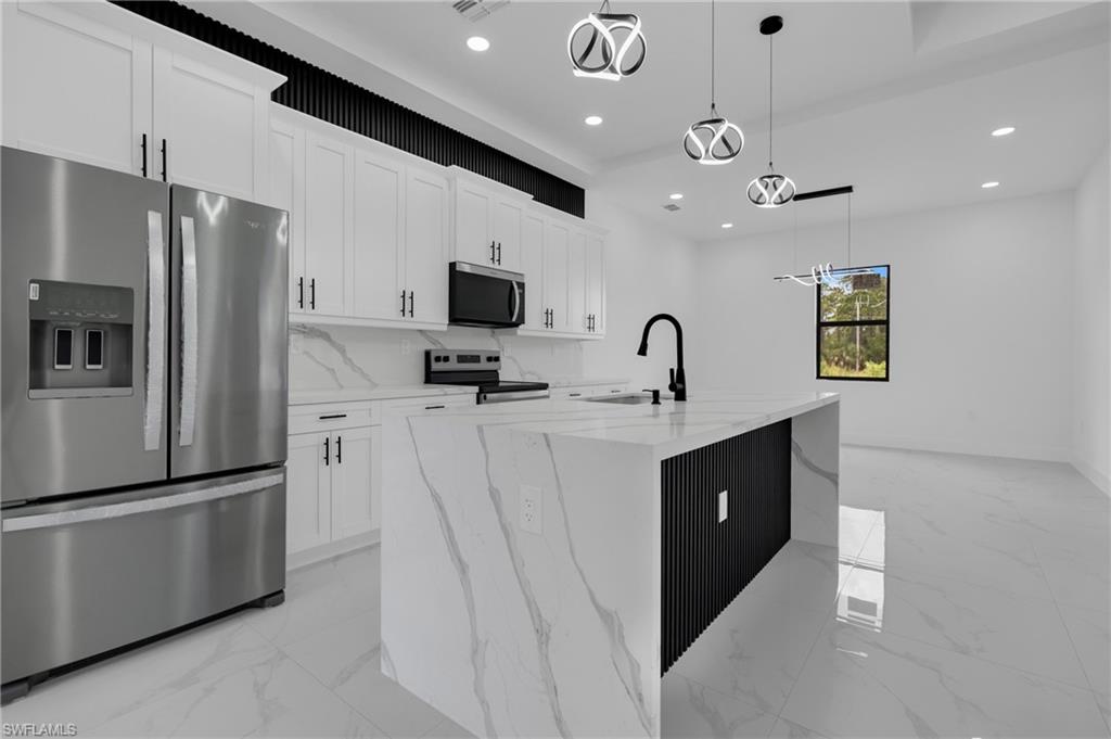 Modern kitchen featuring white shaker cabinetry, stainless steel appliances, a large center island with a waterfall countertop, and contemporary pendant lighting