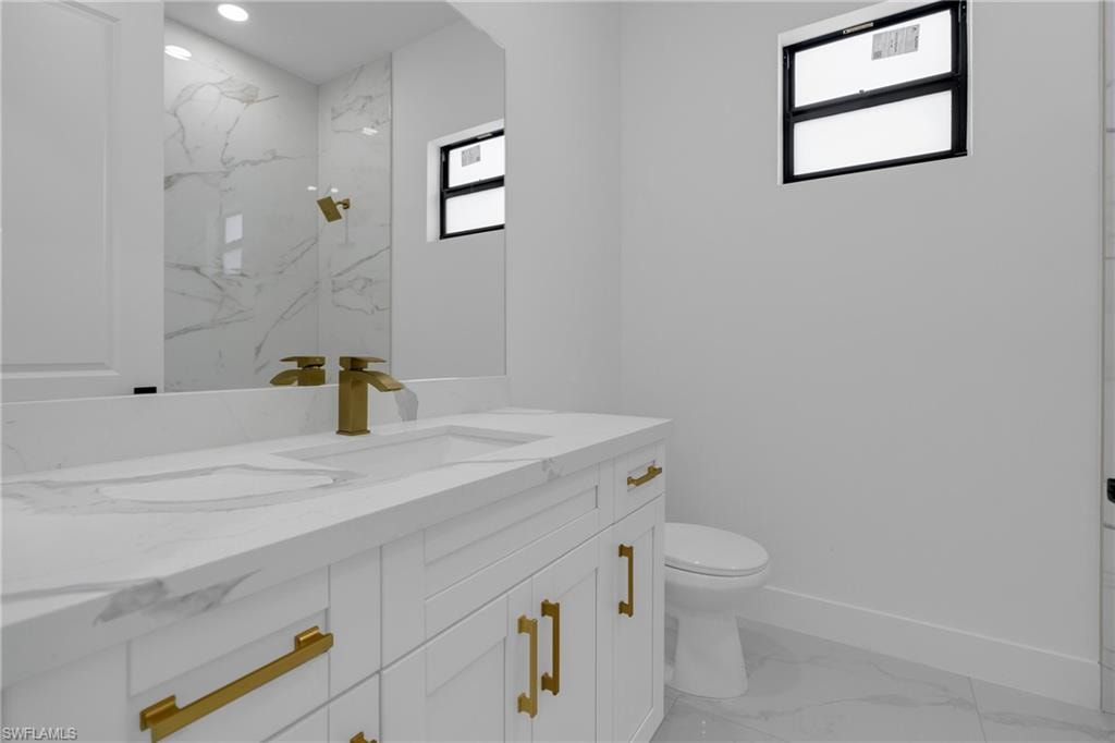 Modern bathroom featuring a white vanity with gold-tone hardware, an integrated sink with a waterfall-style gold-tone faucet, and a large mirror