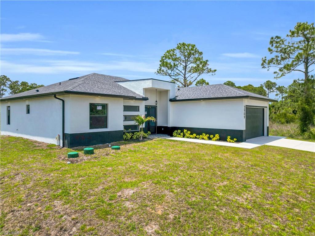 Contemporary single-story residence featuring a white stucco exterior with a dark base, a dark asphalt shingle roof, an integrated garage with a dark door, and a concrete driveway