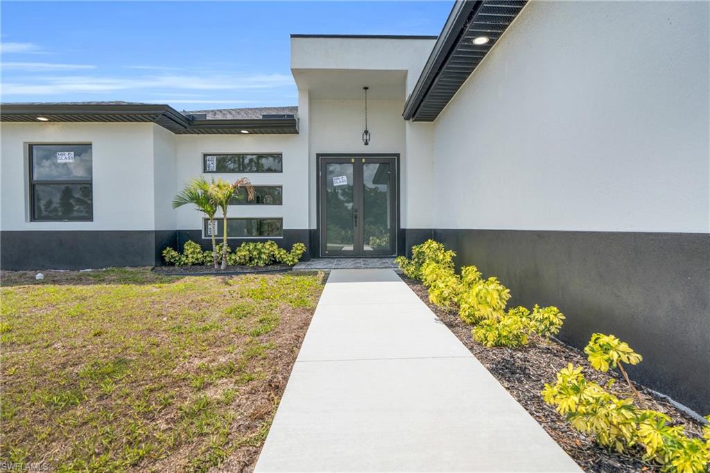 Contemporary exterior featuring a two-tone facade, prominent entry with double glass doors, a concrete pathway, and decorative landscaping