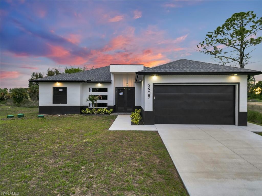 Contemporary single-story residence featuring a two-tone exterior, a dark shingle roof, an attached two-car garage with a dark door, a concrete driveway, and a concrete walkway