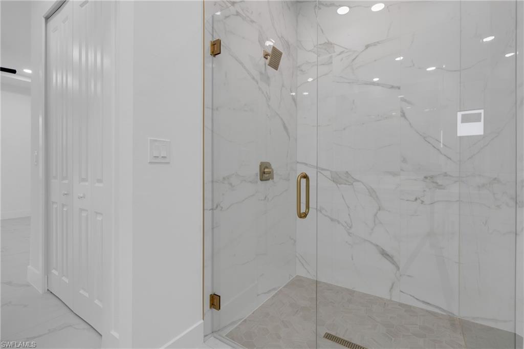 Glass-enclosed shower featuring white marble-look wall tiling, a light gray hex tile shower pan, and gold-tone fixtures