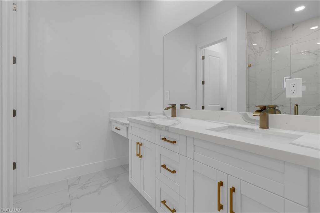 Double vanity featuring white cabinetry with gold-tone hardware, integrated sinks, and a marble-patterned countertop