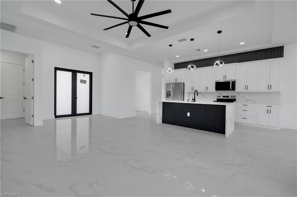 Open-concept living space featuring a contemporary kitchen with white cabinetry, stainless steel appliances, and a central island with a waterfall countertop