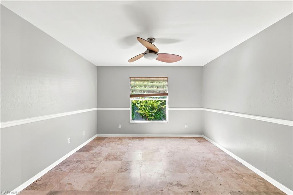 Spacious room featuring neutral grey walls with chair rail molding, a ceiling fan with integrated lighting, and tile flooring