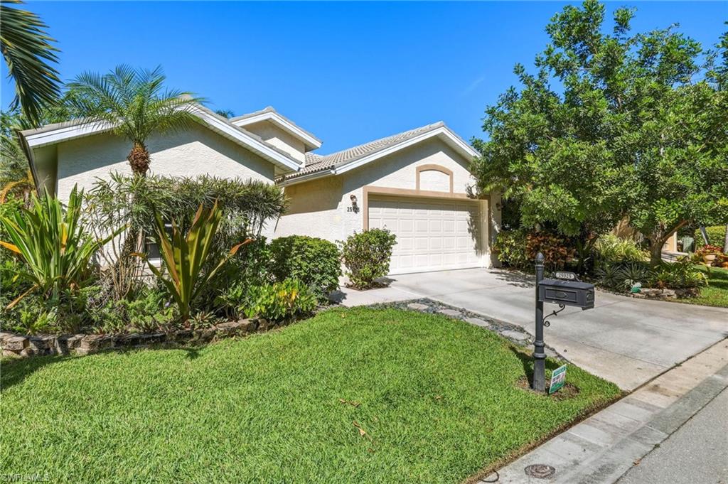 Stucco exterior with a tiled roof, featuring an attached garage, paved driveway, and mature landscaping