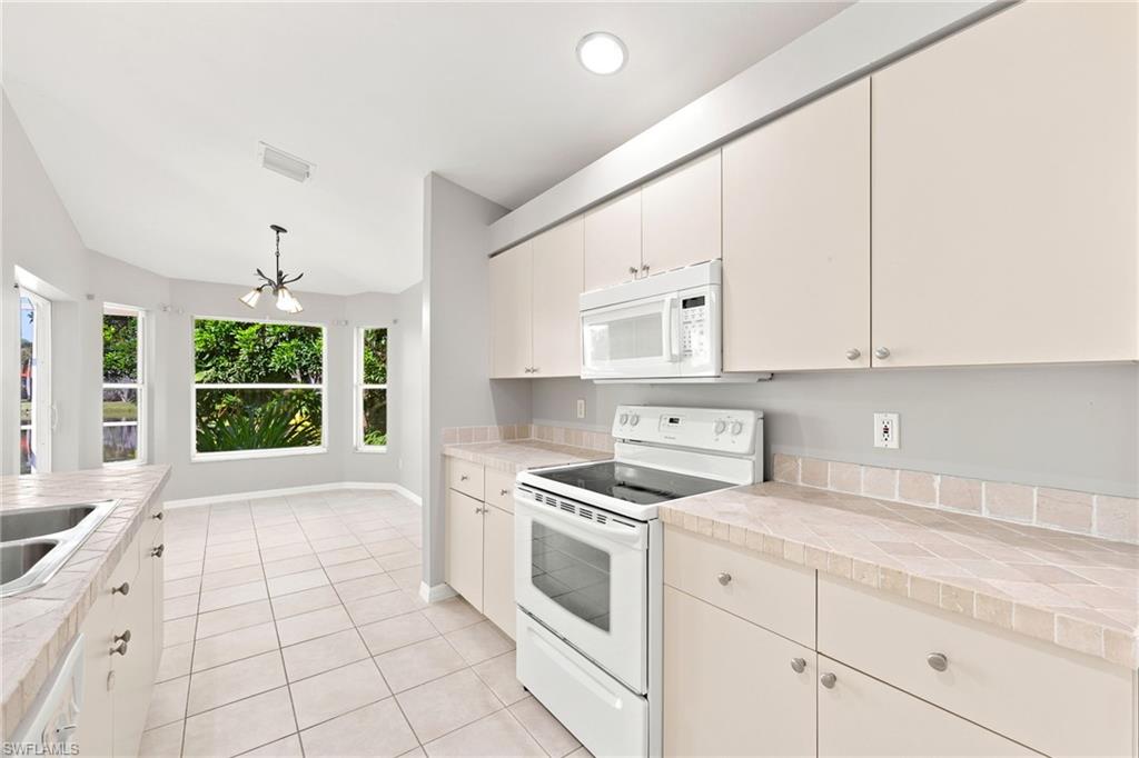 Kitchen featuring white appliances, cream cabinetry with brushed nickel hardware, and tile countertops