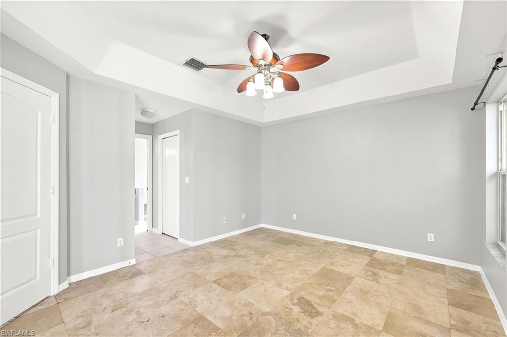 Spacious room featuring tray ceiling with a ceiling fan, light gray wall tones, tile flooring, and white trim throughout
