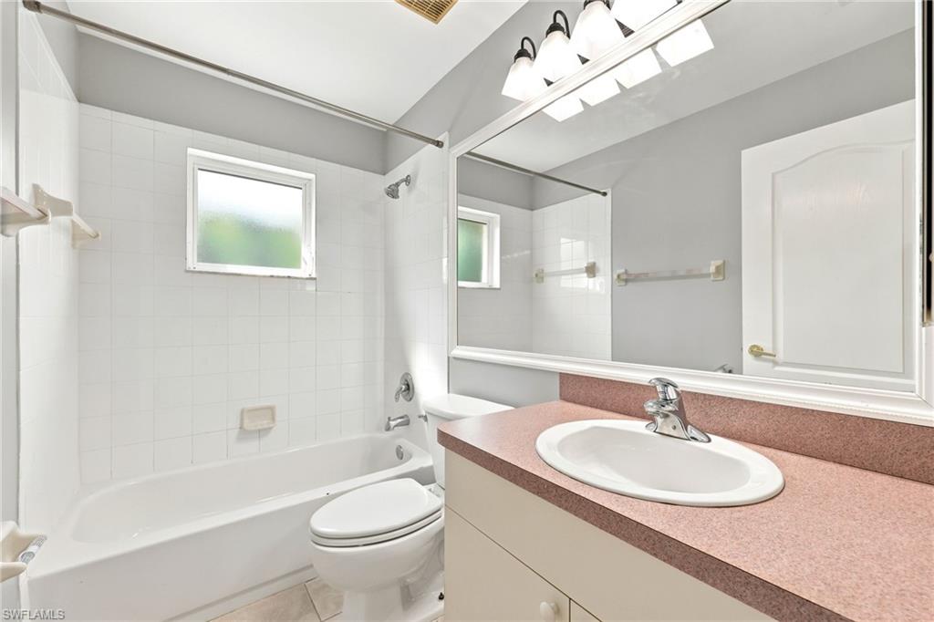 Full bathroom featuring a single vanity with a countertop and undermount sink, a large wall-mounted mirror, and a combined shower and tub with white tile surround